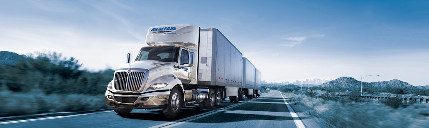 A white Idealease commercial truck rental carrying cargo on the highway during sunrise.